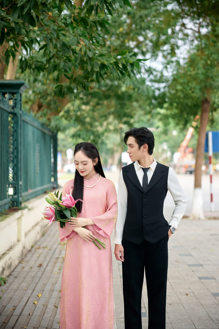 Cặp đôi áo dài hồng đi trên đường có hàng cây