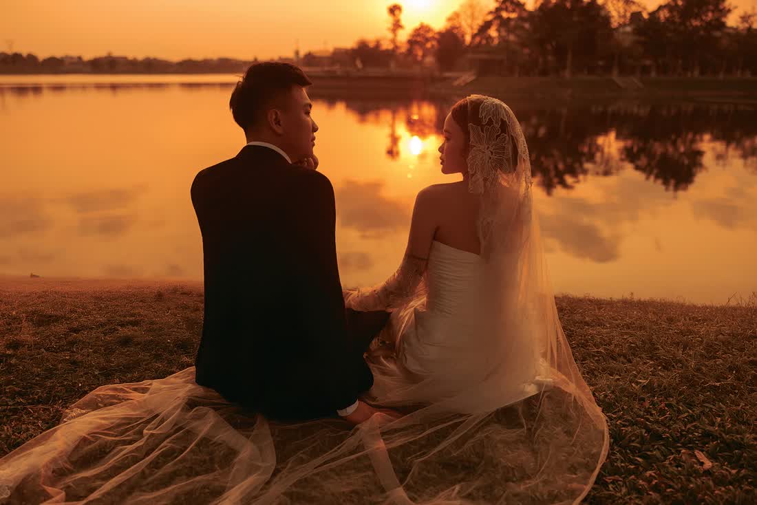 Cô dâu chú rể ngồi bên bờ nước lúc hoàng hôn